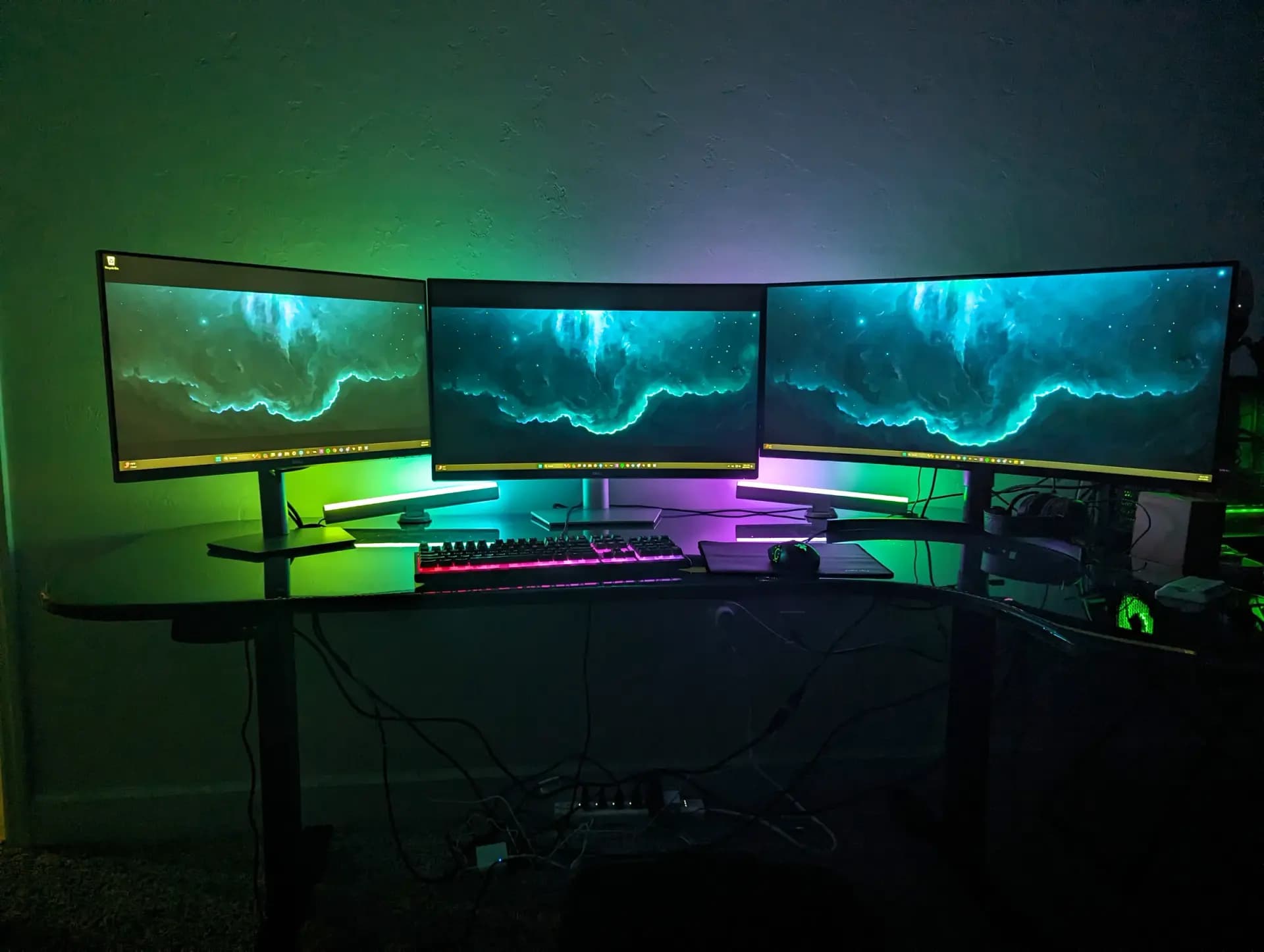 A gaming desk at night with three monitors glowing green and blue